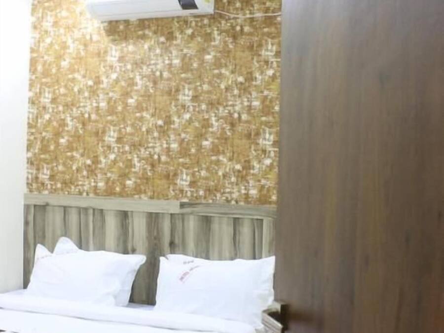 A hotel room with a bed, a ceiling fan, an air conditioning unit, and a wooden door with a number sign.
