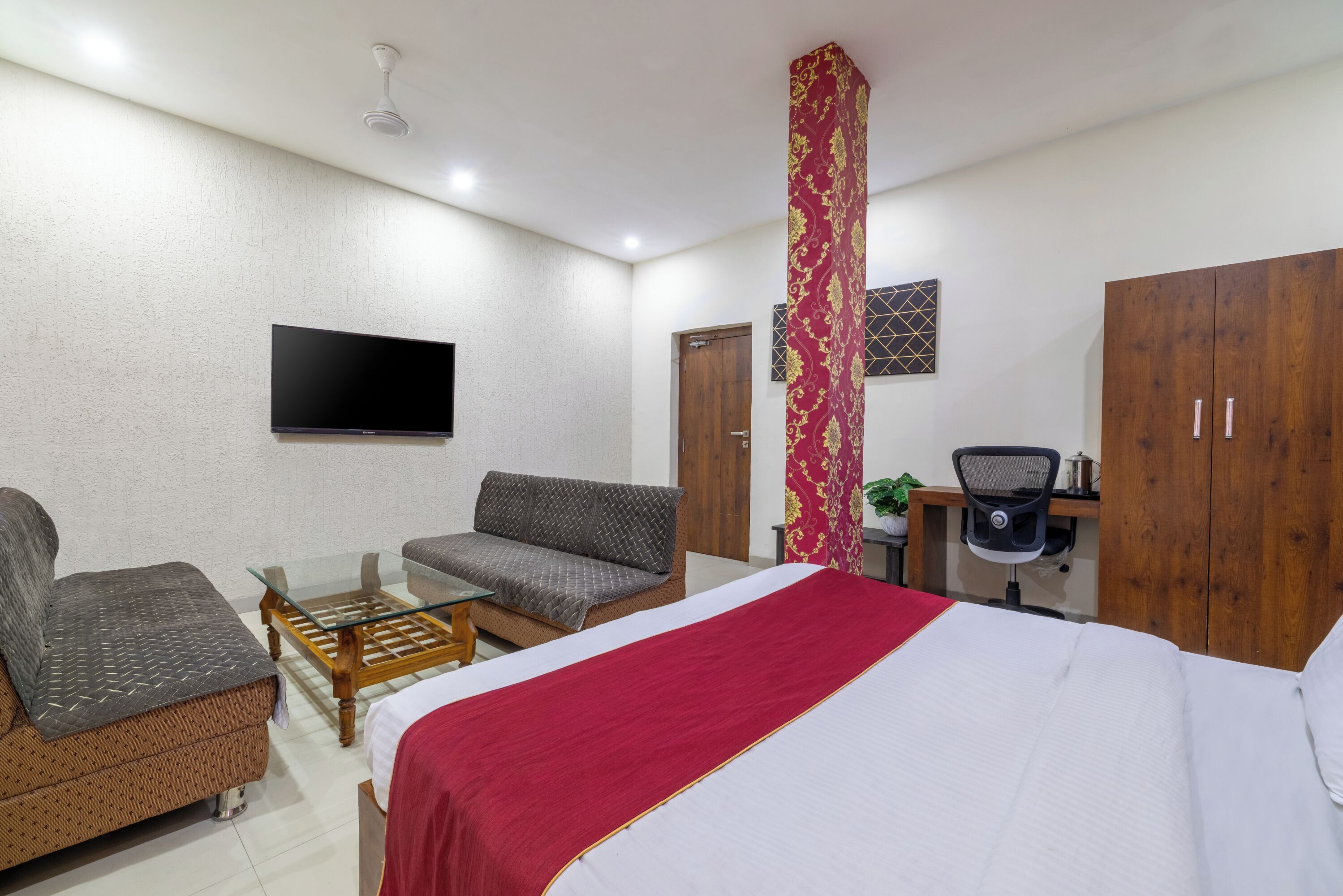 Habitación de hotel con cama, dos sofás, una mesita, un escritorio con silla, televisor y armario.