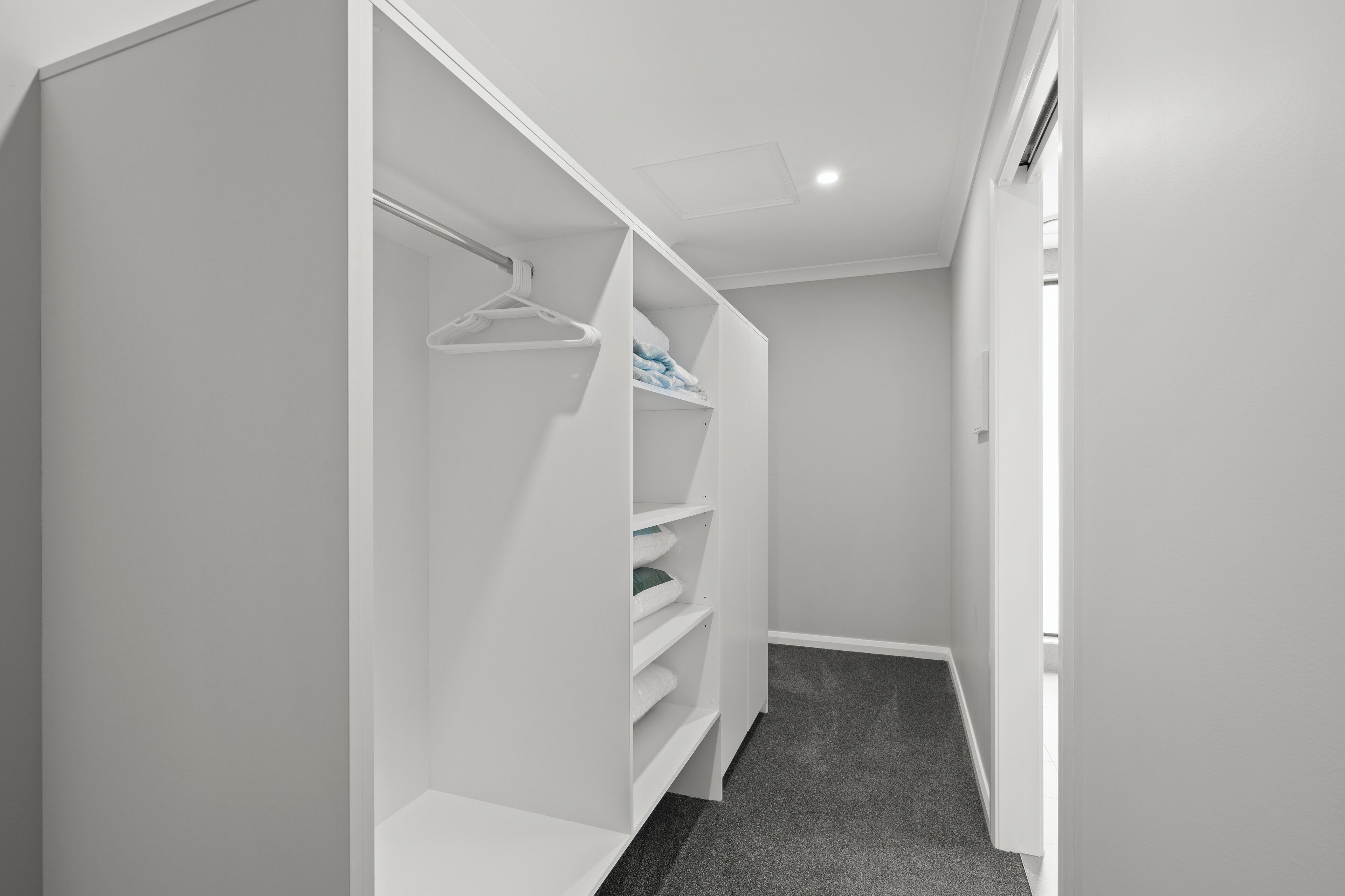 Un couloir étroit avec un placard blanc contenant des étagères et une tringle pour suspendre les vêtements.