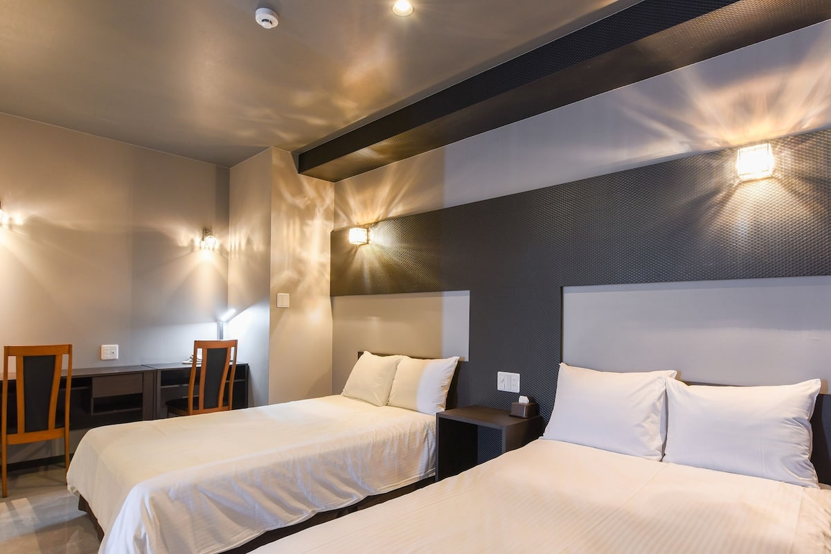 A hotel room with two beds, a desk, and a chair.