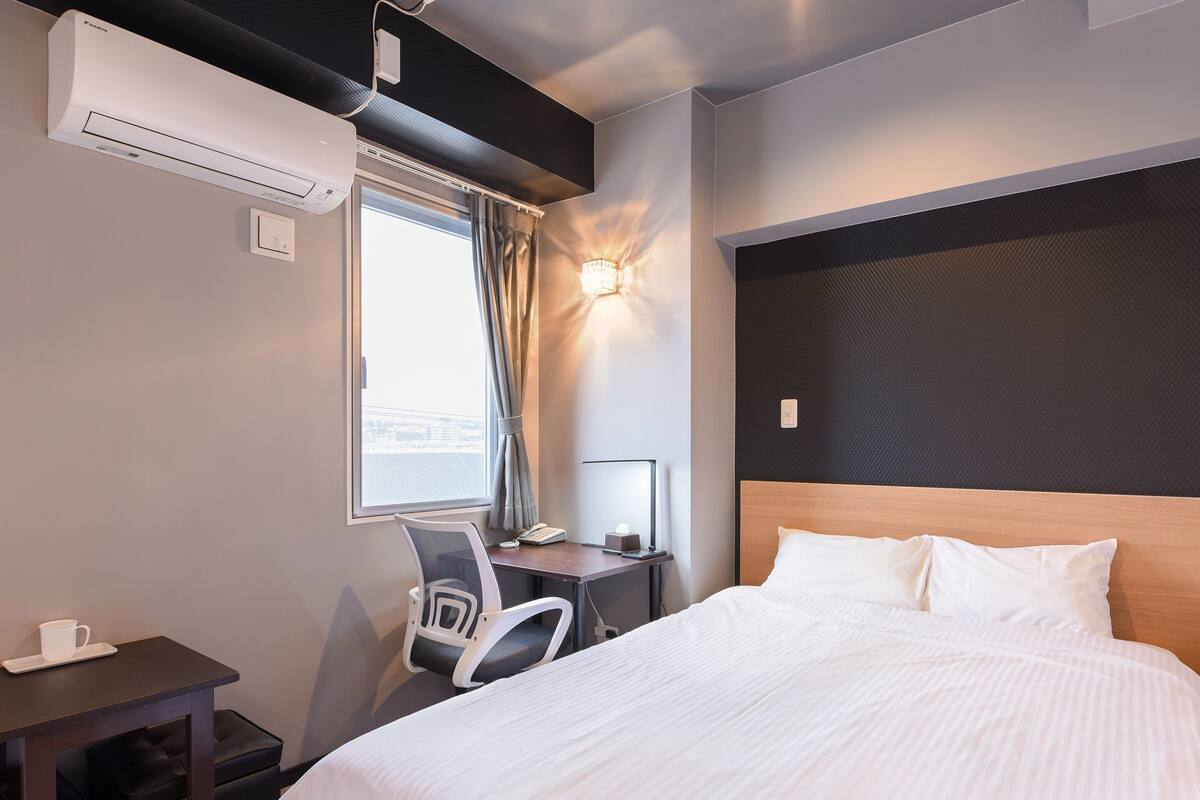 A hotel room with a bed, desk, chair, and a window with curtains.