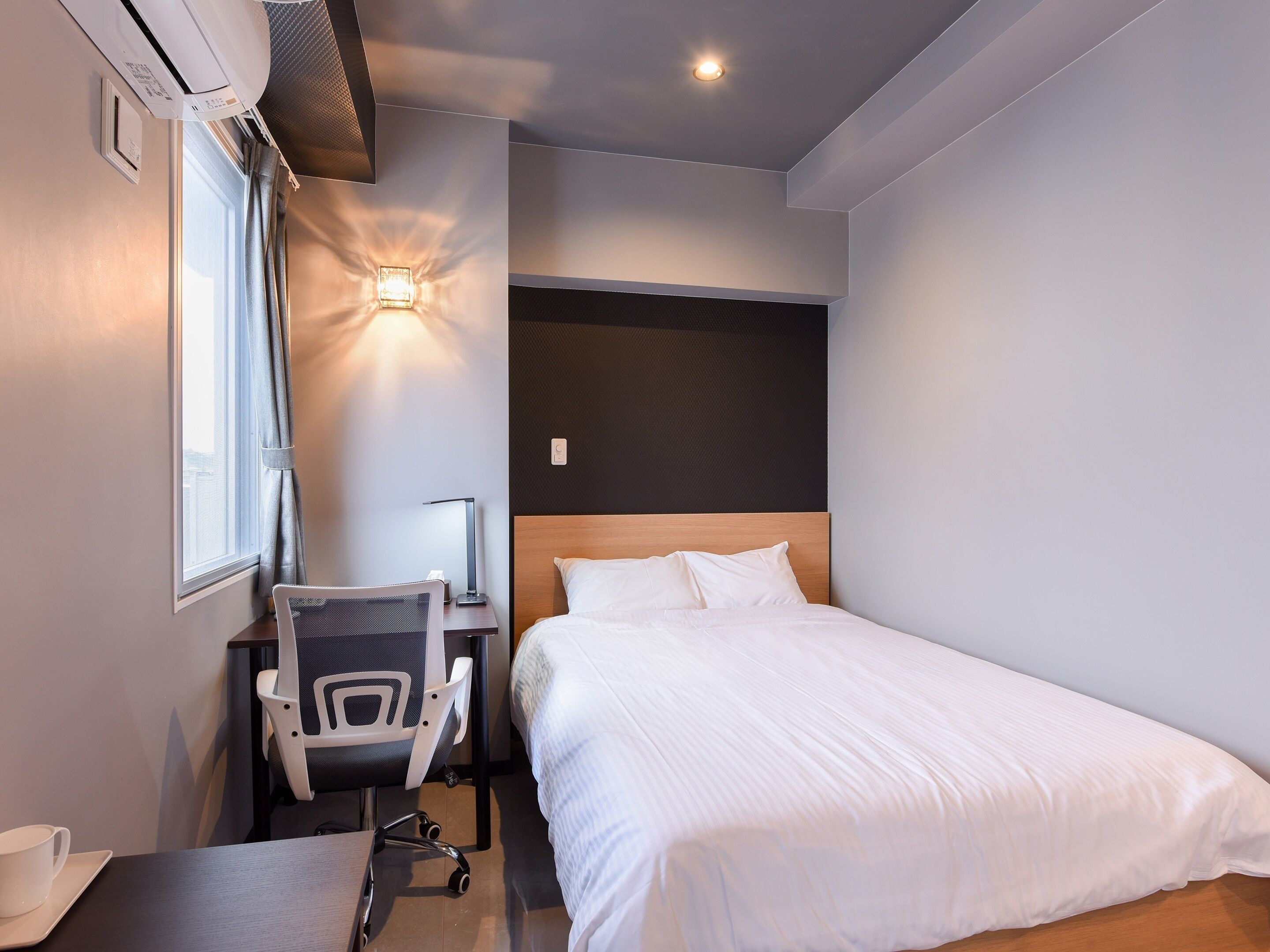 A modern hotel room with a bed, desk, chair, and a window with curtains.