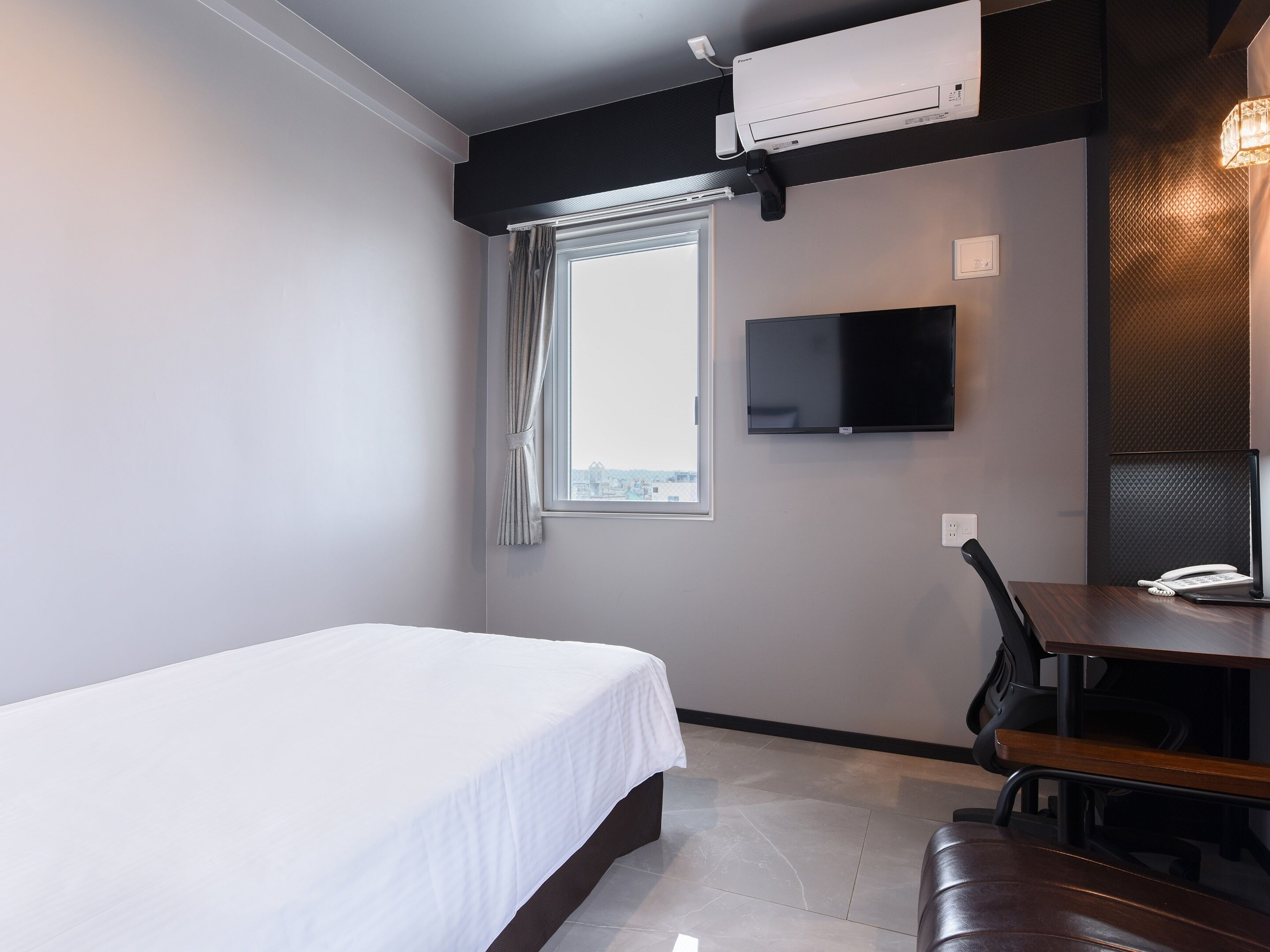 Ein Hotelzimmer mit Bett, Schreibtisch mit Stuhl, Flachbildfernseher und Fenster mit Vorhängen.