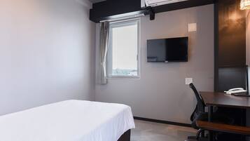 Ein Hotelzimmer mit Bett, Schreibtisch mit Stuhl, Flachbildfernseher und Fenster mit Vorhängen.