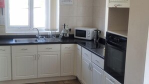Une cuisine avec des meubles blancs, un plan de travail noir, un four à micro-ondes, un évier et une cuisinière.