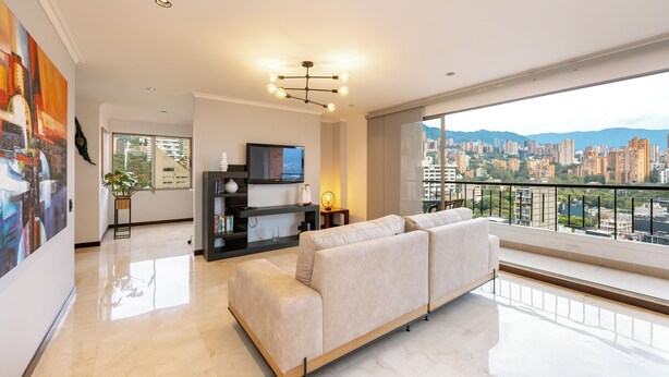 A modern living room with a sofa, a TV, and a large window overlooking a cityscape. - Spectacular 3BR flat with great view close to Provenza (Medellín)