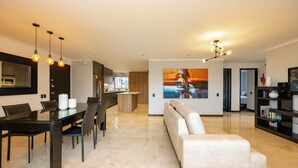 A modern living room with a sofa, dining table, and chairs. There is a kitchen area with a microwave and cabinets. A painting is on the wall, and a bookshelf is visible. - Spectacular 3BR flat with great view close to Provenza (Medellín)