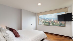 A bedroom with a large bed, a city view through a window, and a mounted TV. - Spectacular 3BR flat with great view close to Provenza (Medellín)
