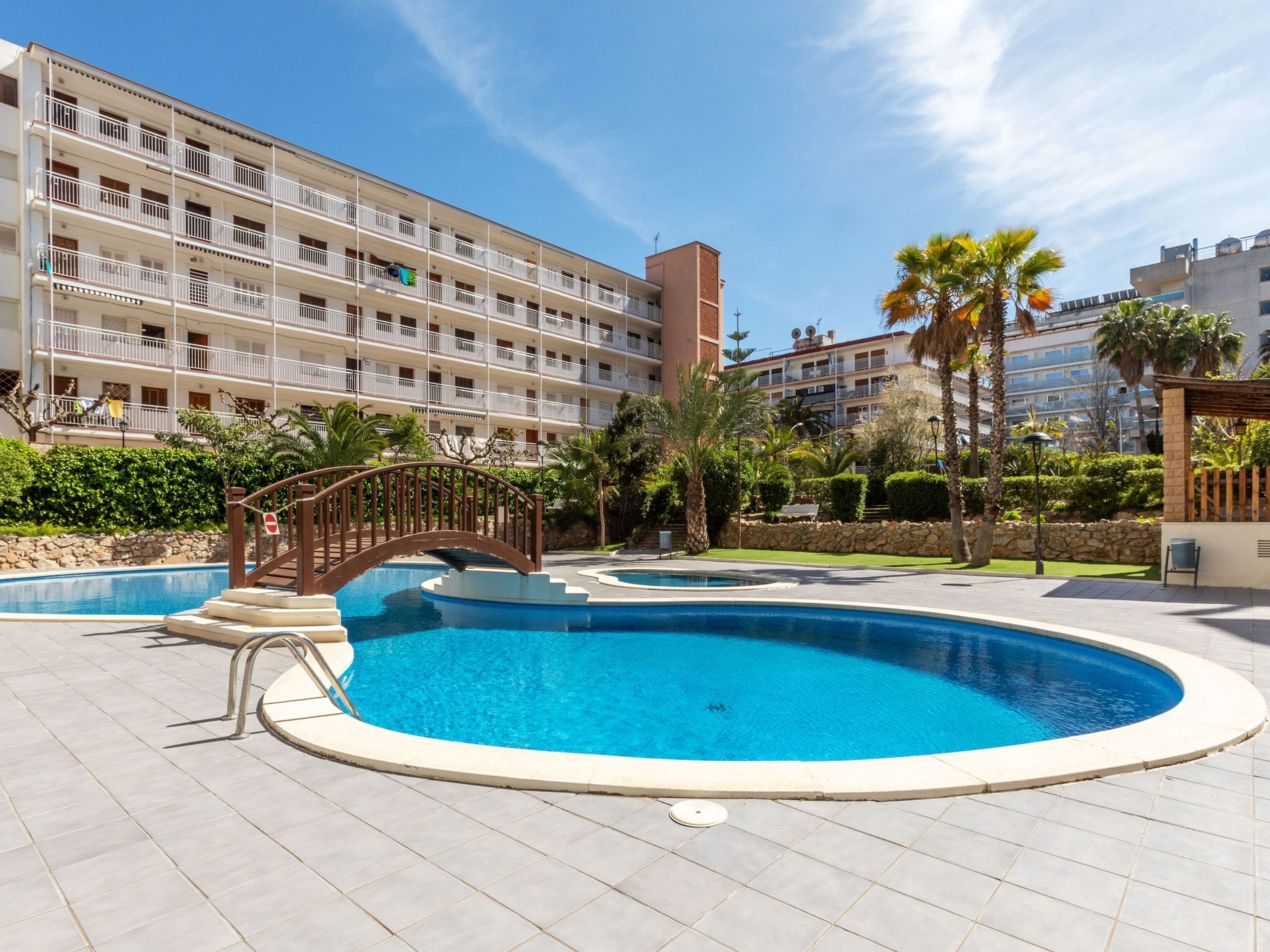 A hotel with a swimming pool, a bridge, and a multi-story building with balconies.