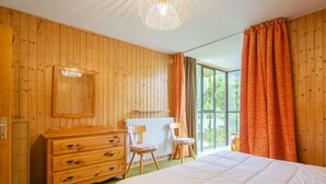 Quarto com painéis de madeira, uma cama, penteadeira, cadeira e uma janela grande com cortinas.