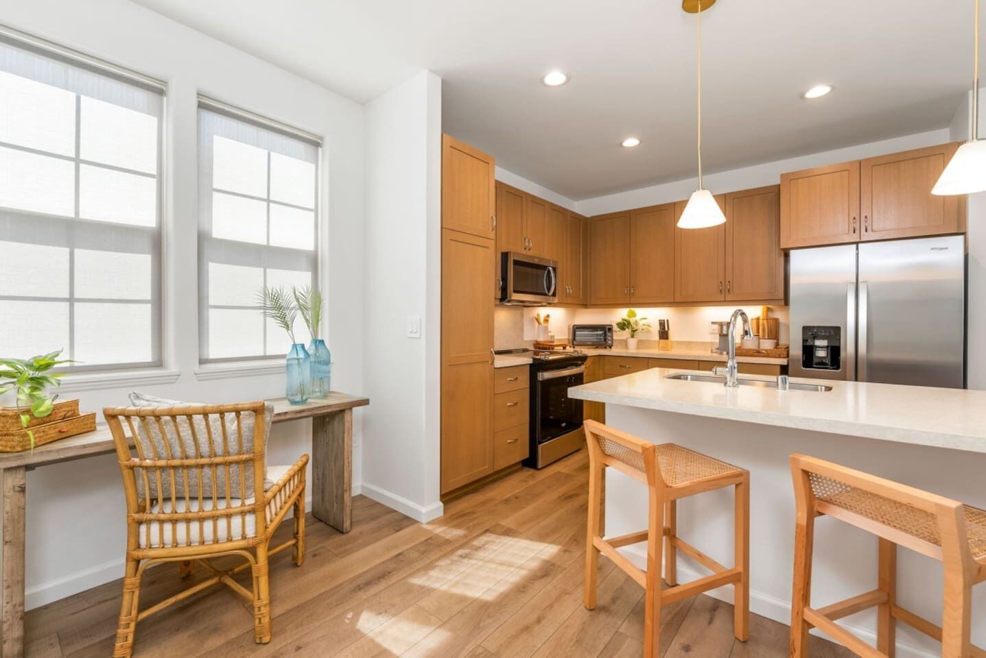 A modern kitchen with wooden cabinets, a stainless steel refrigerator, a microwave, and a large island with bar stools.