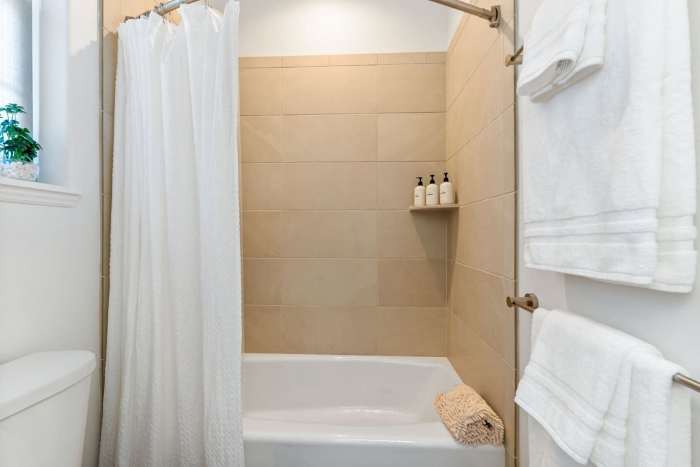 A modern bathroom with a shower, a bathtub, and a toilet. There are white towels hanging on the wall and a shelf with toiletries.
