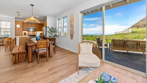 Eine moderne Küche mit Holdekor, ein Essbereich mit Holztisch und -stühlen sowie eine große Schiebeglasdoor, die auf eine Terrasse im Freien mit Blick aufs Meer und die Hügel führt.