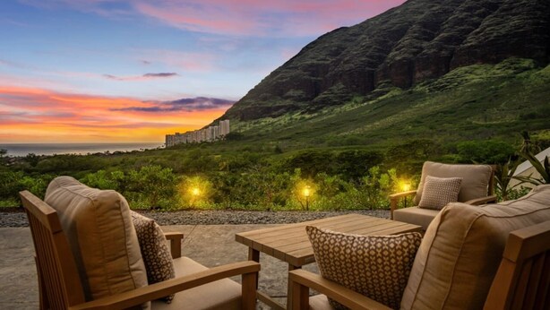 Een terras met houten meubels en uitzicht op een berglandschap in de zonsondergang.