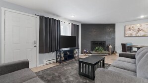 Ein modernes Wohnzimmer mit Flachbildfernseher, grauen Sofas, einem schwarzen Couchtisch und einem Kamin.
