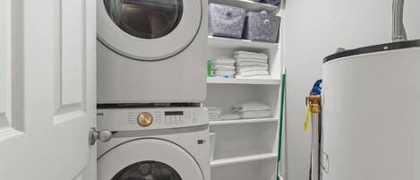 A laundry room with stacked washing machines, shelves with folded towels, and a mop.