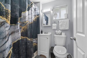 A bathroom with a marble shower curtain, a white sink, a toilet, and a mirror above the sink.