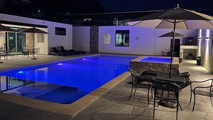 Een buitenzwembad met ligbedden en parasols, omgeven door een moderne patio.