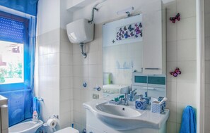 Une salle de bain avec un lavabo blanc, des toilettes et un miroir. Des autocollants décoratifs en forme de papillons ornent le mur.