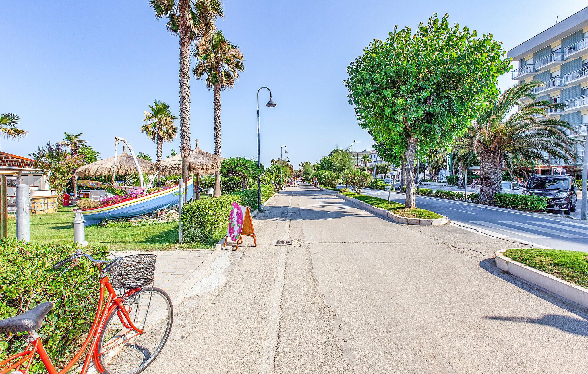 Una calle bordeada de palmeras, una bicicleta y una estructura con techo de paja.