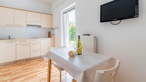 A modern kitchen with wooden cabinets, a dining table with a white tablecloth, a rose decoration, and a bottle of wine. - Lavrič Studio 1 at Lake Bloke, Bloke, Slovenia (Bloke)