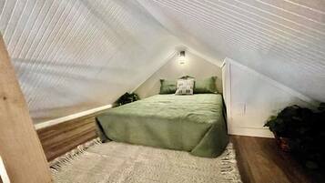 Ein kleines Schlafzimmer im Dachgeschoss mit geneigter Decke, einem Bett, Kissen und einer Nachttischlampe.