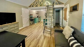 A spacious living room with a TV, a sofa, and a dining area with a kitchen in the background. - The Eclectic - "Treehouse" and "Bunkhouse" (Bryan)