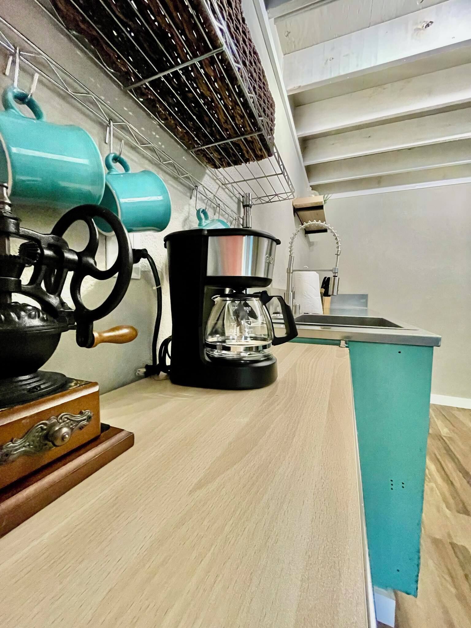 Een keuken met een koffiezetapparaat, een waterkoker en een spoelbak.
