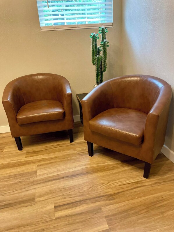 Two brown leather armchairs with dark legs, positioned on a wooden floor against a beige wall. - The Eclectic - "Treehouse" and "Bunkhouse" (Bryan)