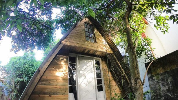 Una cabaña de madera con techo triangular, una puerta blanca y una ventana.