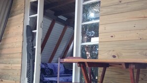 Una terraza de madera con una mesa y un banco, una puerta corrediza de vidrio y vistas del interior.