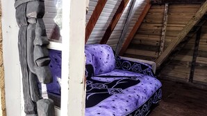 Una habitación con techo inclinado, vigas de madera, un ventanal y un sofá morado con estampado.