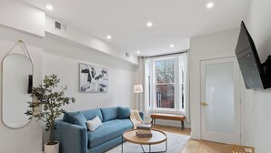 A modern living room with a blue sofa, a round coffee table, a potted plant, and a large window providing natural light.