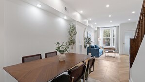 A dining area with a wooden table and chairs, a potted plant, and a blue sofa in the background.