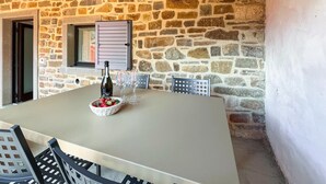 A stone wall exterior with a table set for two, featuring a bottle and a bowl of strawberries.