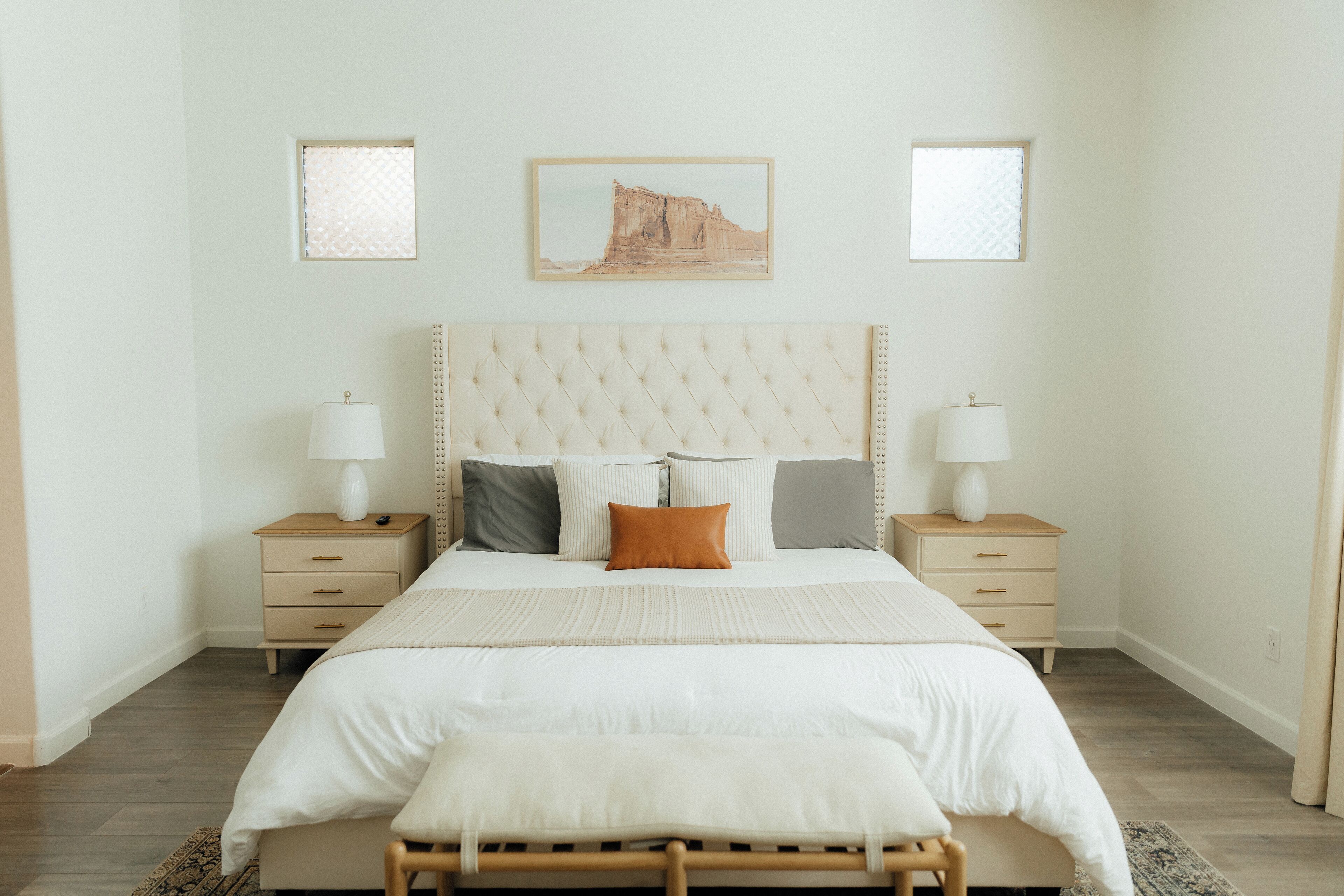 Une chambre à coucher bien rangée, avec un grand lit, deux tables de chevet, une tête de lit et un tableau encadré au mur.