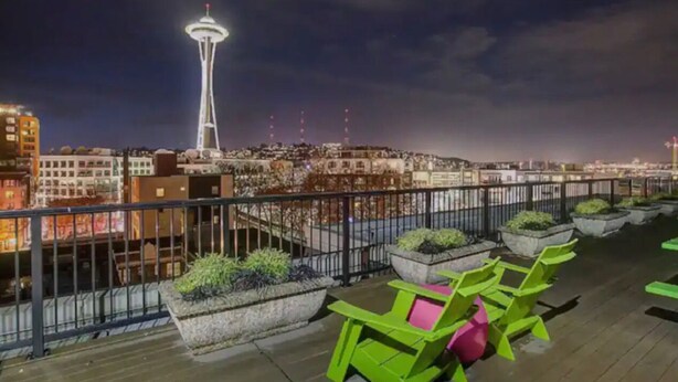 Une terrasse sur le toit avec des sièges extérieurs, une vue sur la Space Needle et un panorama de la ville illuminée la nuit.