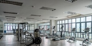 Un gimnasio amplio con diversos equipos de ejercicio, ventanas grandes y un techo alto.