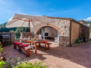Ein Gebäude aus Stein mit einer Ziegelterrasse, Sitzmöglichkeiten im Freien, einem Grill und einem Fernseher im Hintergrund.