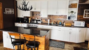 Una cocina con armarios blancos, encimera negra, una isla de madera con taburetes de bar y una araña.