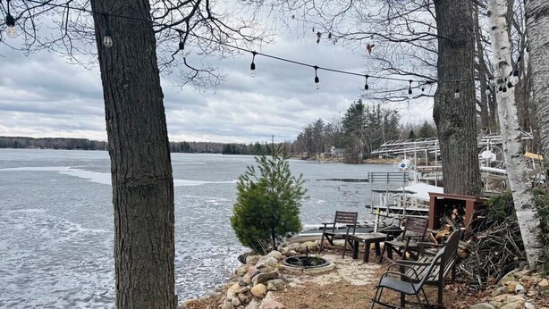 Un patio junto al lago con suelo de piedra, mobiliario exterior y una chimenea.
