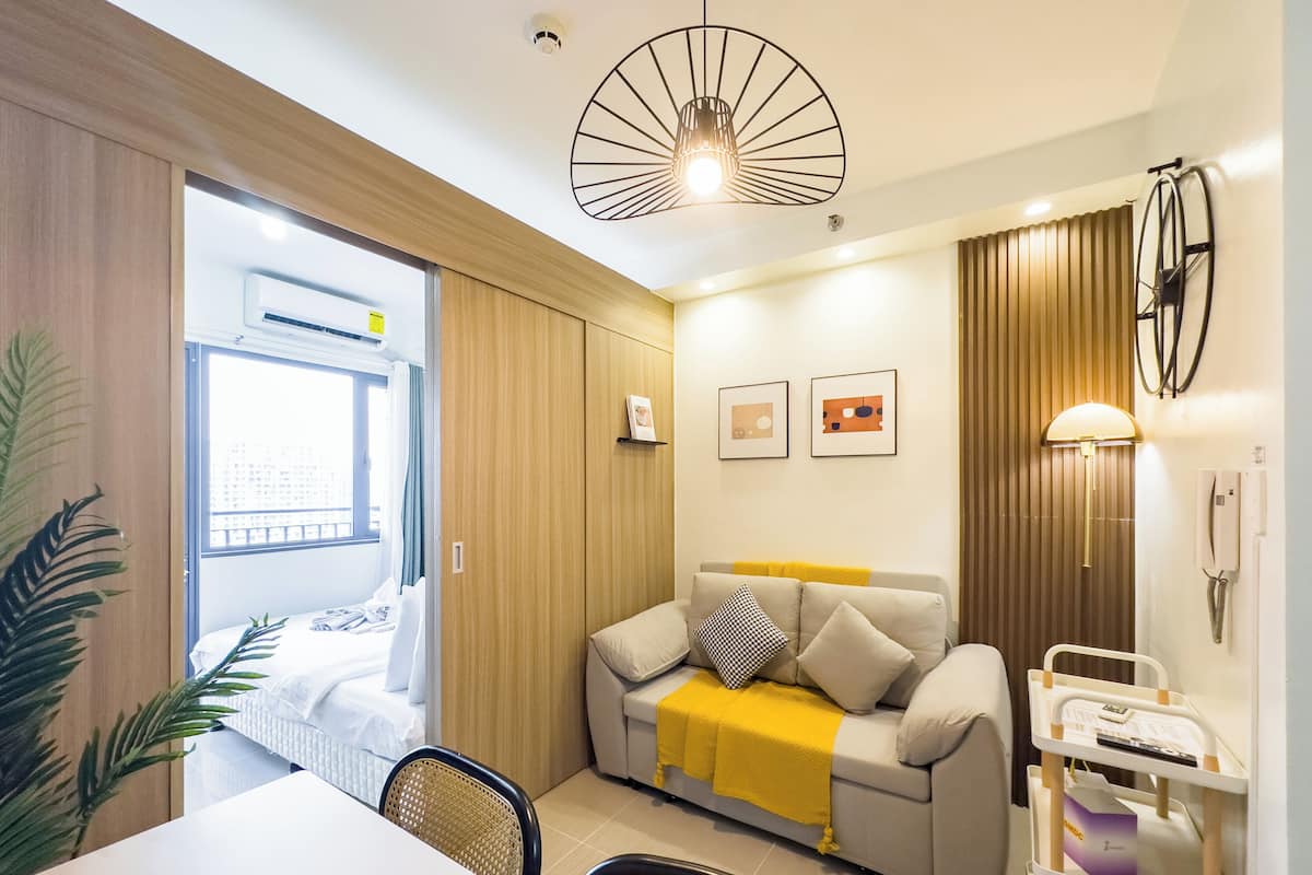 Una habitación de hotel moderna con sofá, mesa de comedor, sillas, una mesita auxiliar, teléfono en la pared y una lámpara en el techo.