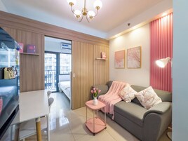 A modern hotel room with a sofa, a small table with a vase of flowers, a desk, and a wardrobe.