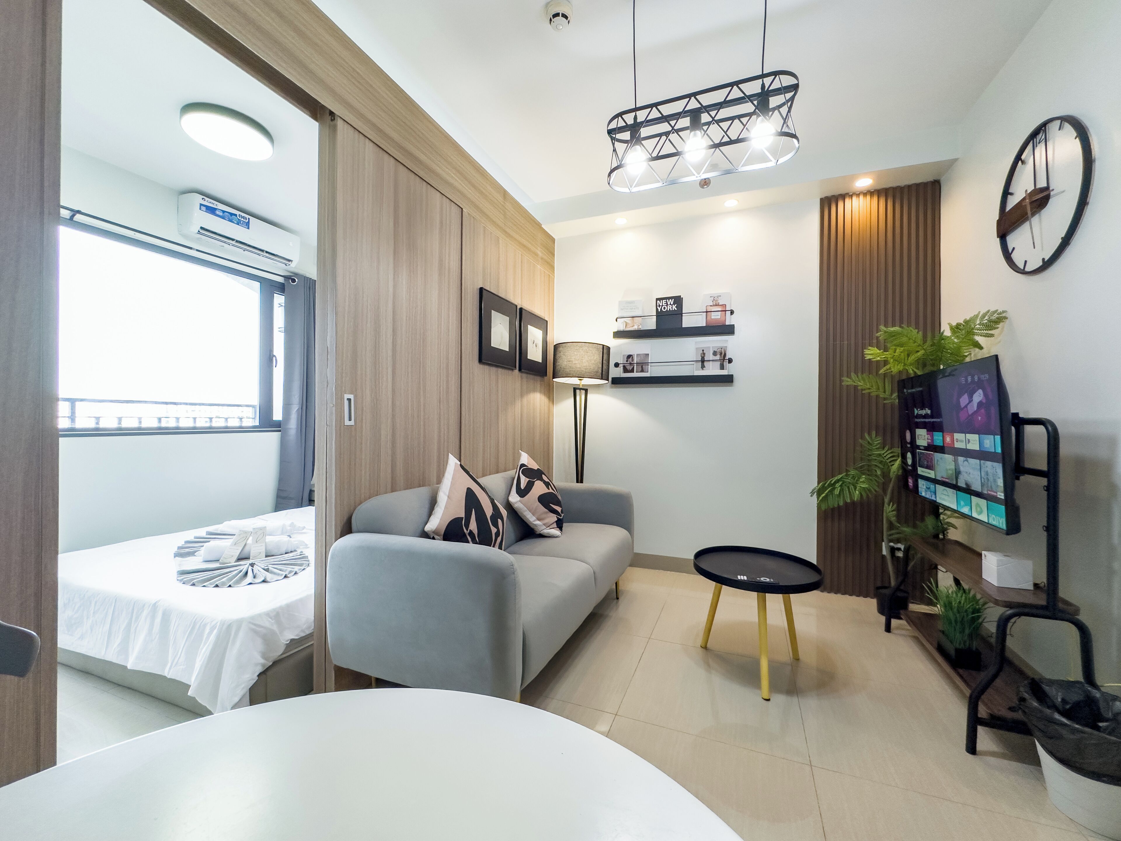 Un salon moderne avec un canapé, une petite table ronde, un téléviseur à écran plat fixé au mur et un luminaire suspendu au plafond.
