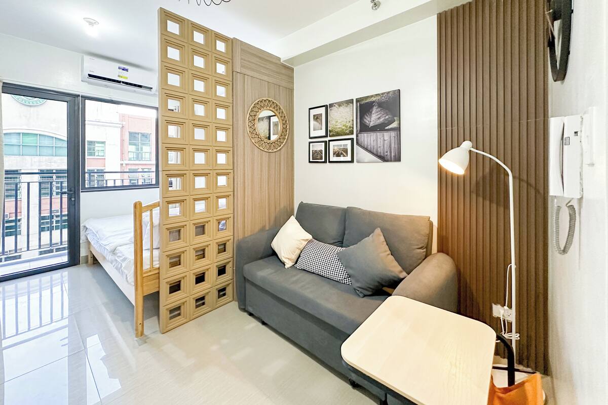 Una sala moderna con un sofá gris, un separador de madera, una mesita y una lámpara de pie.