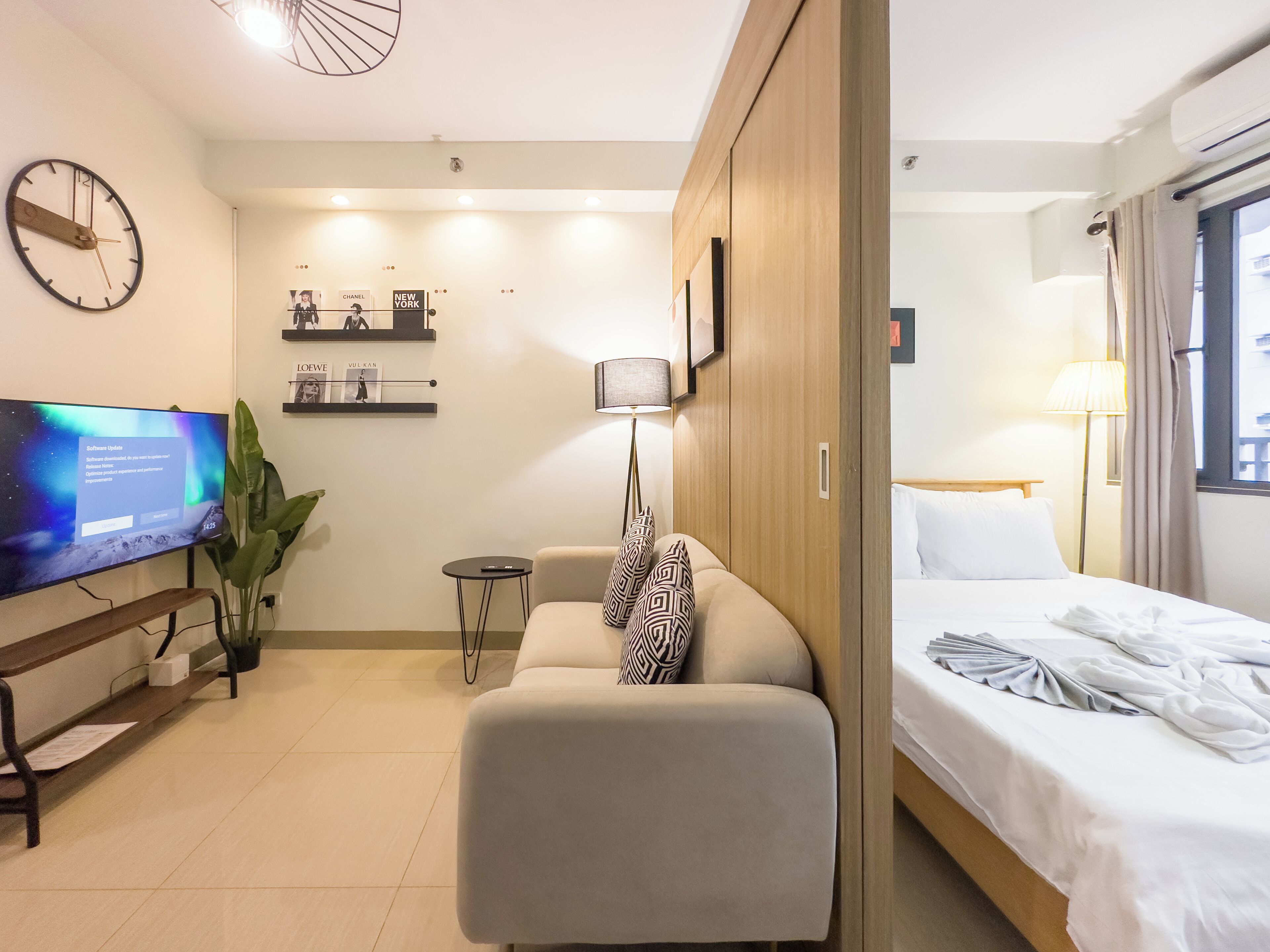 Ett modernt hotellrum med en säng, en soffa, en TV, ett litet bord och en växt.