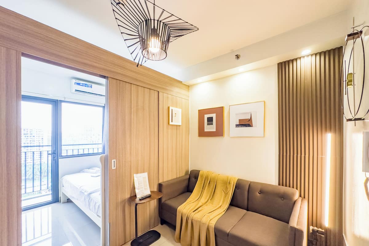 Una habitación de hotel moderna con cama, sofá, una mesita y un ventanal grande.