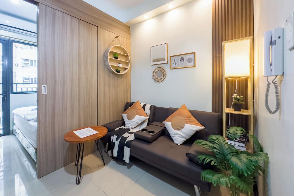 Una habitación de hotel moderna con un sofá, una mesita, una planta en maceta y un teléfono de pared.