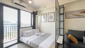 Ein modernes Schlafzimmer mit Bett, Sofa, Balkon und Blick auf die Stadt.