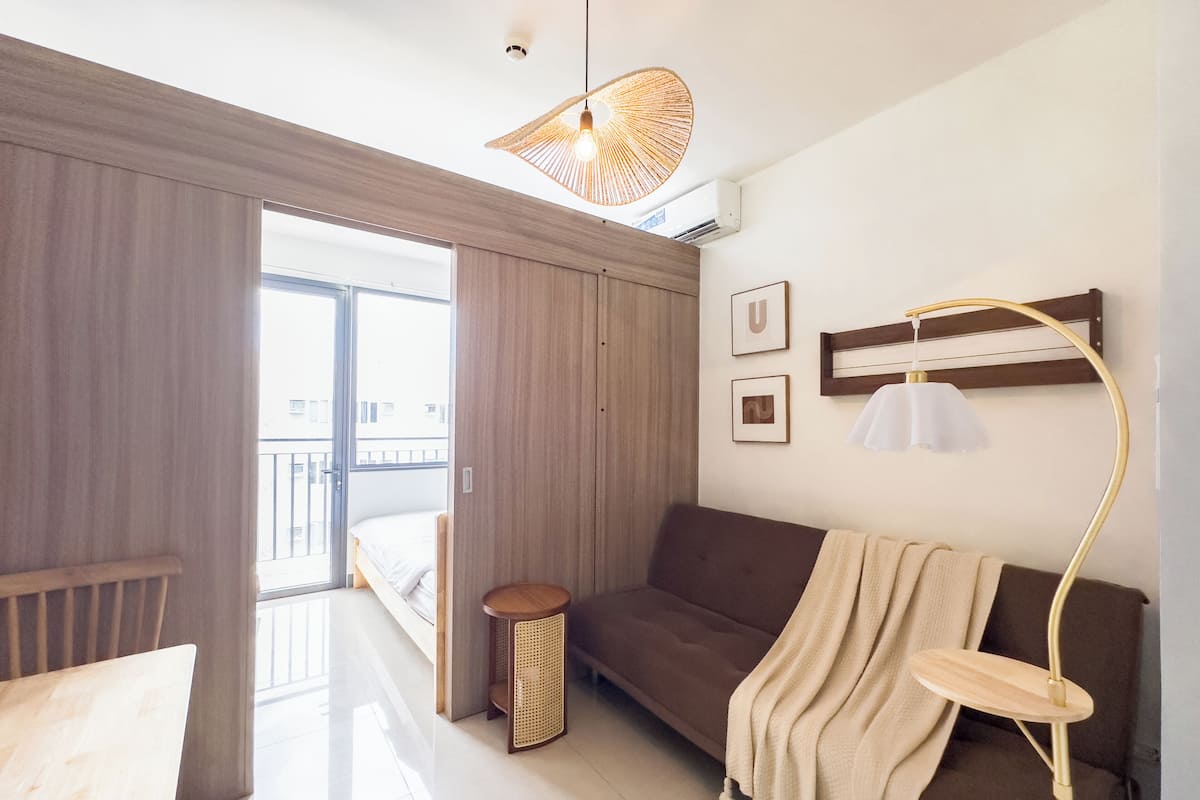 Una habitación de hotel moderna con un sofá, una mesita auxiliar, una lámpara de pie y un ventanal con vistas al exterior.